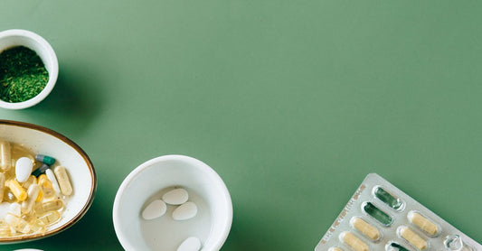 Frasco de Femin Plus cápsulas sobre una mesa blanca con hojas verdes, representando un suplemento multivitamínico natural para mujeres.